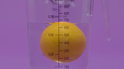 Orange floating in water inside a measuring jug