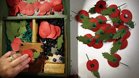 A box of paper poppies being constructed by a hand