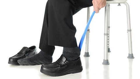 An elderly man sliding into his loafers with the aid of a long-handled shoe horn.