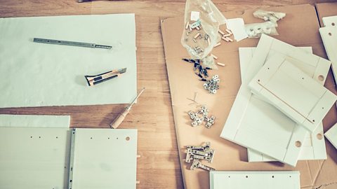 Flat-pack furniture parts laid out on the floor with instruction sheets and tools.
