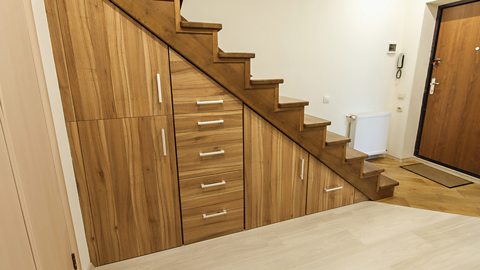 A modern, wooden, built-in storage space with cupboards and drawers underneath a staircase.