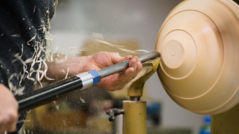 A worker’s hands shown turning wood to shape it with a tool on a bowl lathe.