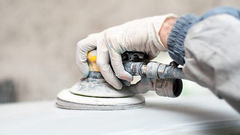 A gloved hand using a buffing machine to polish a car for painting.