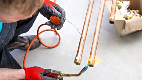 A gloved plumber is shown brazing three copper tubes.