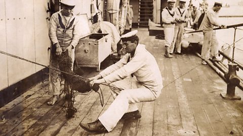 Two sailors working on a net while others watch on a ship in World War One