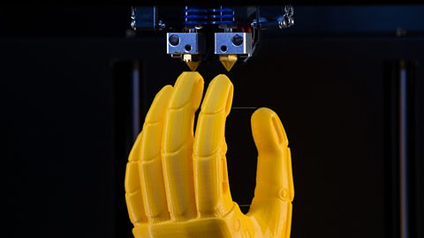 A yellow plastic model of a prosthetic hand being 3D printed.