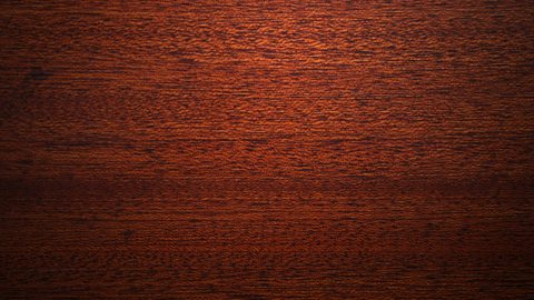 The texture of mahogany wood - very dark red brown with a darker grain running through.