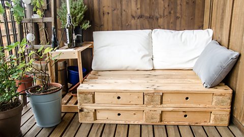 Wooden pallets reused as a bench, shown with cushions on and drawers in the gaps.