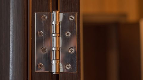 A metal, square butt hinge uses eight screws to hold a cupboard door in place.