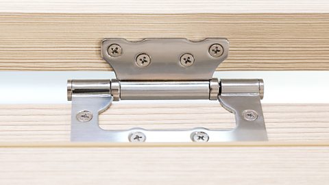 A metal, square flush hinge uses eight screws to hold a cupboard door in place.