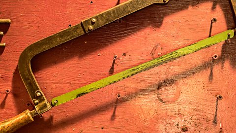 A yellow hacksaw hung on small nails against a red wooden wall.