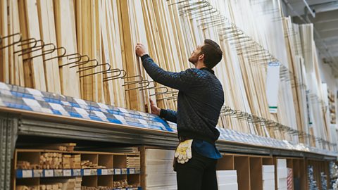 A man in a DIY store is selecting from a variety of strips of timber.