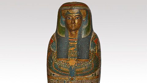 A photograph of a human mummy case with a painted body and a gilded face