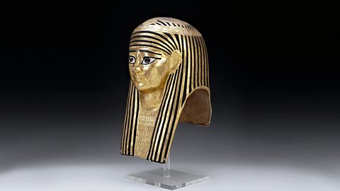 A photograph of a human mummy mask coated in gold leaf
