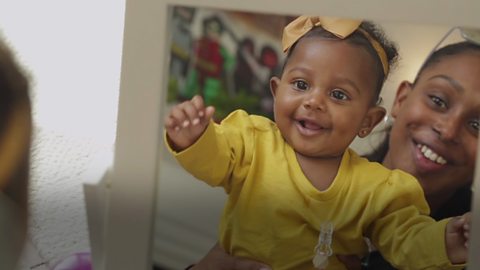 Mum holding baby girl up to a mirror