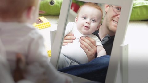 A baby boy and his father reflected in the mirror.