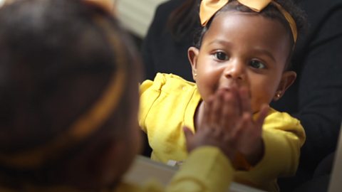 A baby girl reaching out to her own reflection in a mirror.