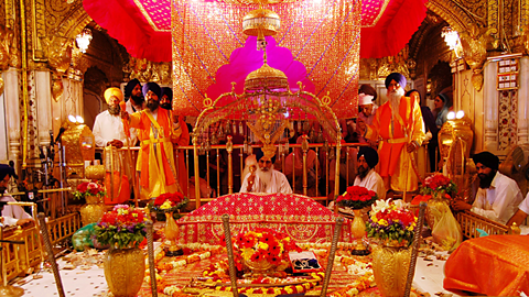 A Sikh priest sits behind the Guru Granth Sahib holy book in the Gurdwara