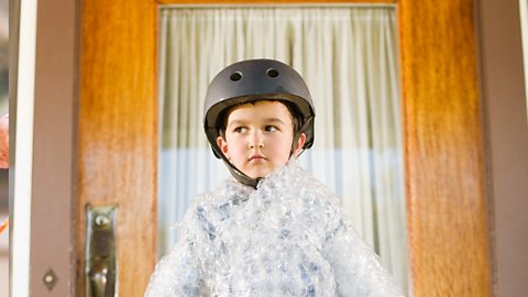 A little boy wrapped in bubble wrap and wearing a crash helmet.