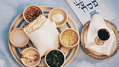 A birds-eye view of a table setting for a dinner. There is a plate containing different food items, including a single chicken bone and a single egg. There is also a small goblet containing a dark liquid inside. 