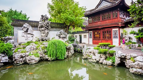 A red house in a garden next to a pond with fish