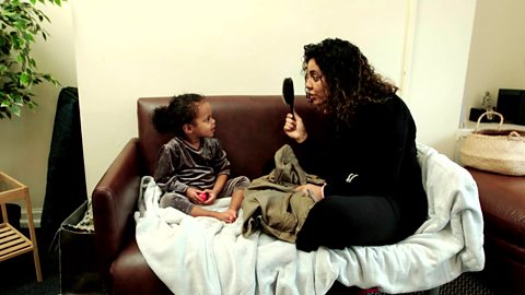 A mum holding up a brush and saying 'brush' to her daughter.