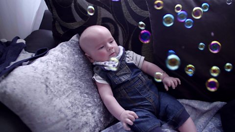 A baby watching bubbles in the air.