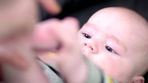 A baby boy looking at his feet as his mum touches his toes.