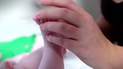 A mum's hand touching a baby's toes.