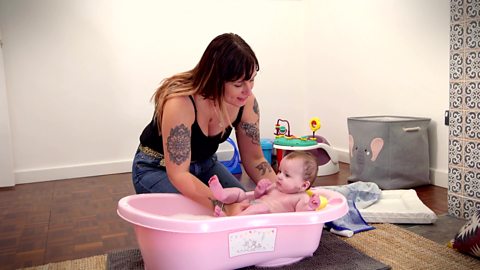 A mum lowering her baby son into the bath.