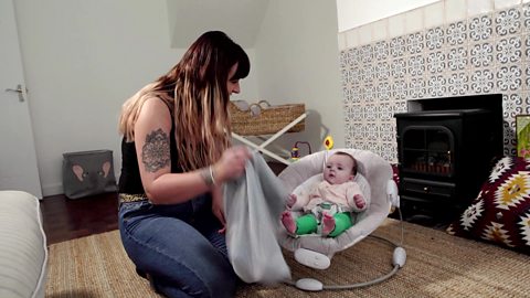 A mum holding a pillowcase in front of her baby daughter.