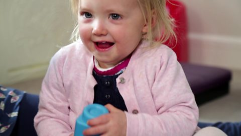 A little girl looking mischievous holding a building block.