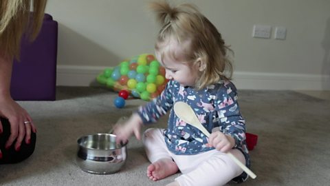 A little girl playing with a saucepan and wooden spoon.