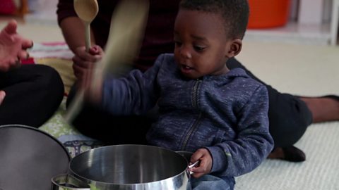 A little boy hitting a pan with a wooden spoon.