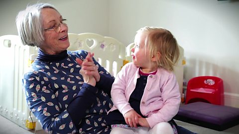 A grandma singing a nursery rhyme to her granddaughter on her lap.