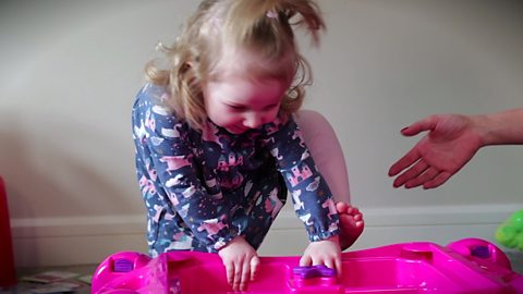 A little girl climbing over a toy.