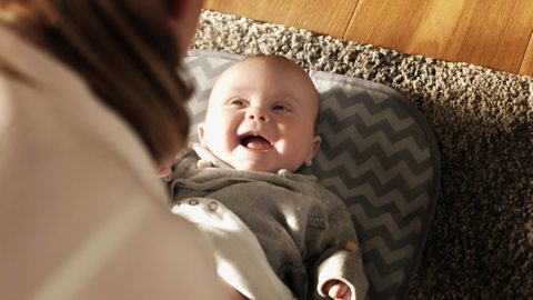 A young baby smiling back at their mum.