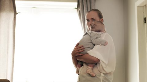 A mum holding a baby to her chest and talking. 