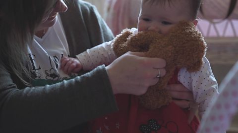 A mum tickling her daughter under the chin with a teddy.