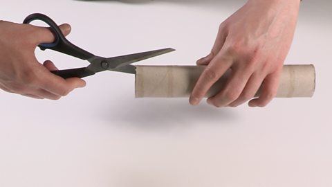 Cutting slots in one end of a kitchen roll tube using scissors.