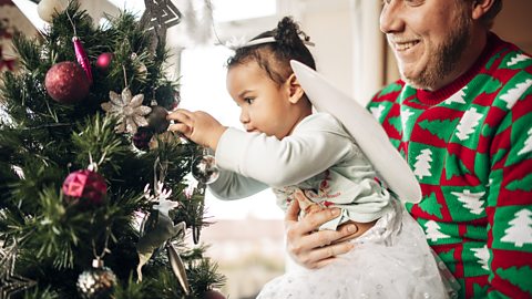 A young girl hangs decorations on a Christmas tree with help from her dad.