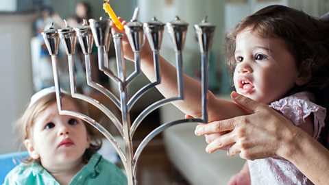 Two young children light candles on a menorah.