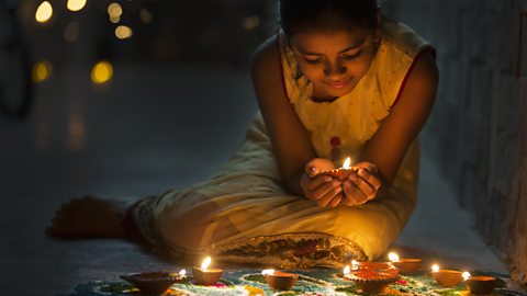 Young girl celebrating Diwali.  She is surrounded by candles and is holding one in cupped hands.