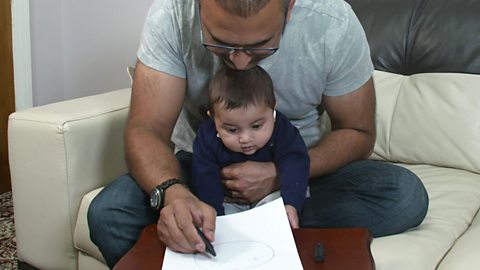 A dad talking to his baby son about his drawing of a face.