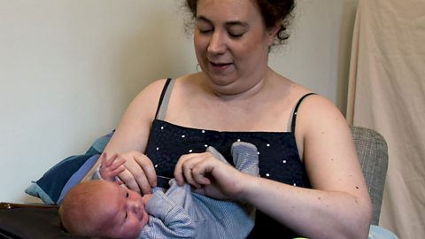 A mum talking to her baby as she dresses him.