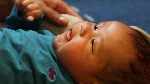 A mum's hand touching her baby son's cheek with a soft blanket.