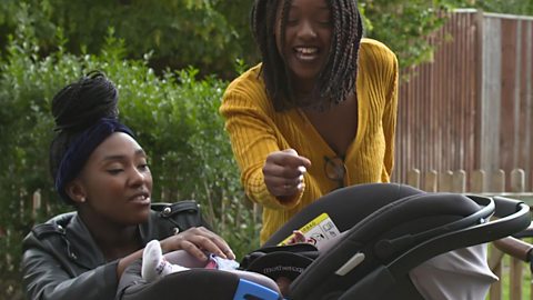 A mum and her sister talk over baby in pram.