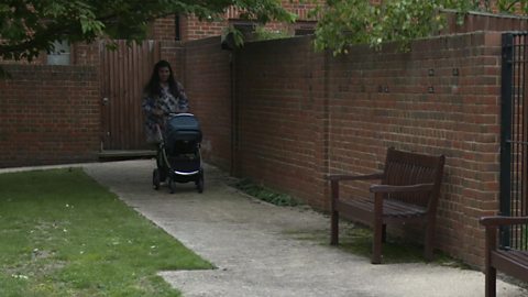 A mum pushing a pram through a green part of an estate.