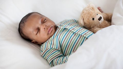 Newborn baby sleeping in a stripy babygrow with a teddy