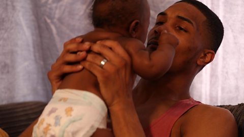 A dad cuddling his baby in a vest top.